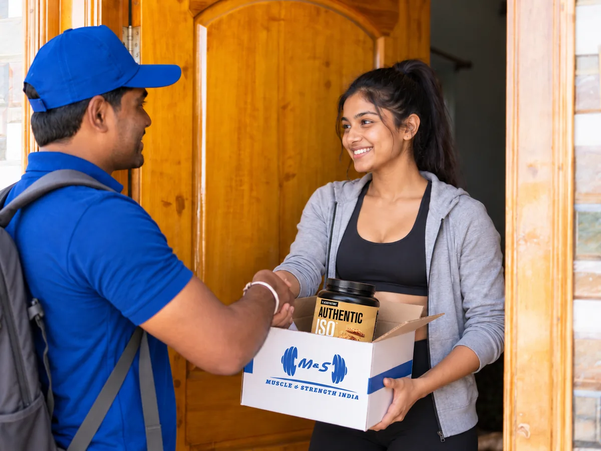 Delivery rider handing a Muscle & Strength India box to a customer at her door
